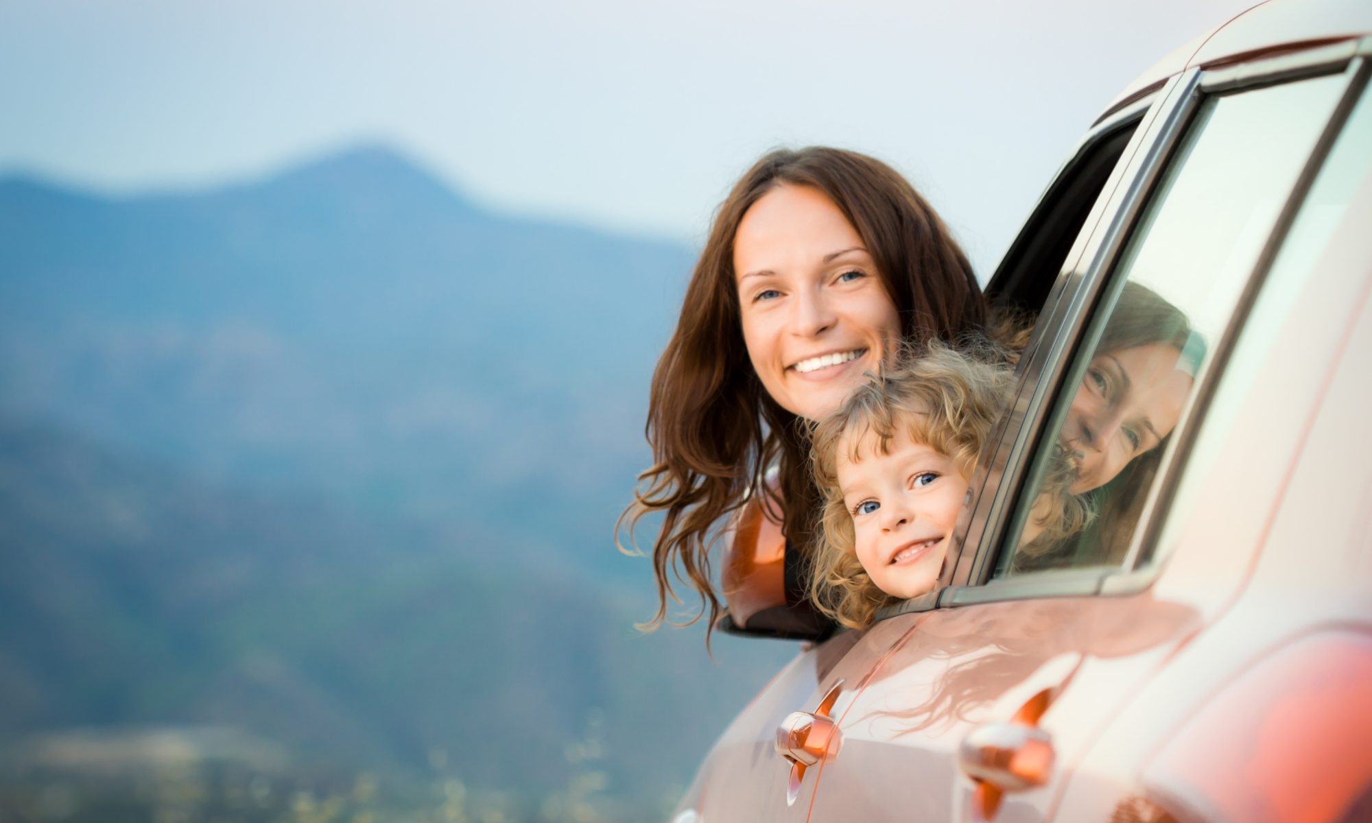 Woman and child sticking their head out of a car window in the countryside