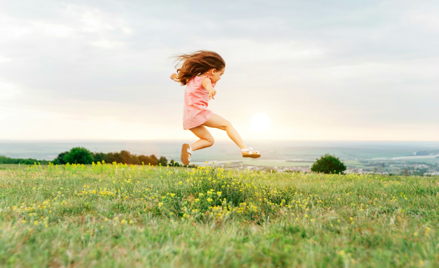 Young girl in a pink dress jumping through a field with yellow flowers, more fields in the distance - and why the countryside should be on your 2021 UK travel list